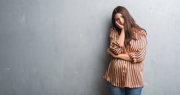 Young brunette woman over grunge grey wall thinking looking tired and bored with depression problems with crossed arms. - Foto, imagen