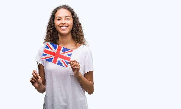 Young hispanic woman holding flag of United Kingdom with a happy face standing and smiling with a confident smile showing teeth - Photo, Image