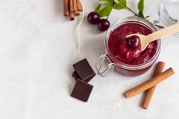 Homemade cherry jam with chocolate, spices (cinnamon, nutmeg) with fresh cherries in a jar on a light background. - Foto, immagini