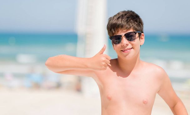 Маленька дитина у відпустці на пляжі щаслива з великою посмішкою робить знак ок, великий палець пальцями, відмінний знак
 - Фото, зображення