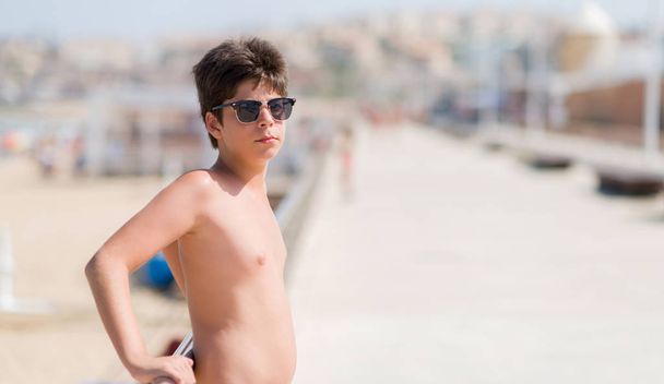Niño pequeño de vacaciones en la playa con una expresión de confianza en la cara inteligente pensando en serio
 - Foto, imagen