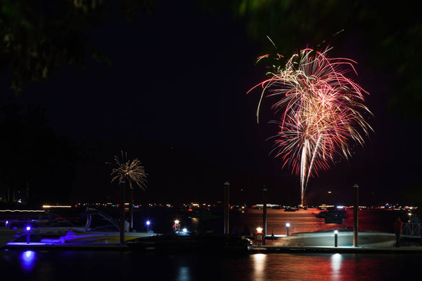 Hermosos fuegos artificiales del 4 de julio brillando sobre el lago Coeur d 'Alene en Idaho con varios barcos abarrotando el agua y el muelle
. - Foto, Imagen