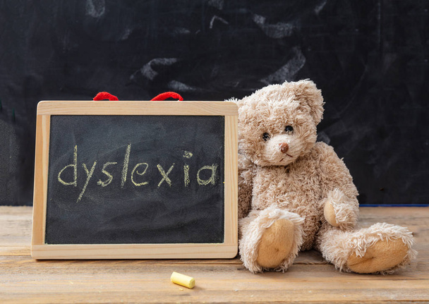 Dyslexia and school. Teddy bear and a blackboard. Dyslexia text drawing on the blackboard - 写真・画像
