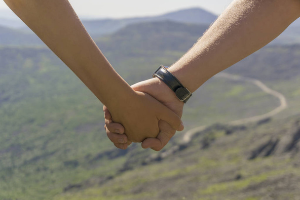 мандрівники чоловік і жінка тримають руки (тільки руки видно крупним планом) на тлі розмитих гірських вершин на відстані
 - Фото, зображення