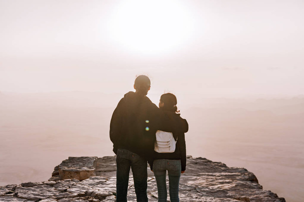 Yalnız genç çift erkek ve kadınların sırt çantası ile İsrail'negev Çölü gündoğumu görünümünü hayran. Genç çift makhtesh uçurumun kenarında duruyor ramon park. - Fotoğraf, Görsel