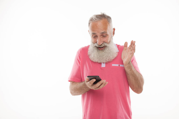 Studio shot of happy senior bearded man smiling while using mobile phone against white background - Photo, image