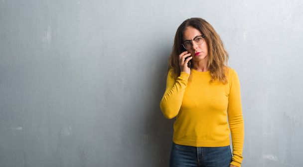 Mujer hispana de mediana edad hablando por teléfono con una expresión segura en la cara inteligente pensando en serio
 - Foto, Imagen