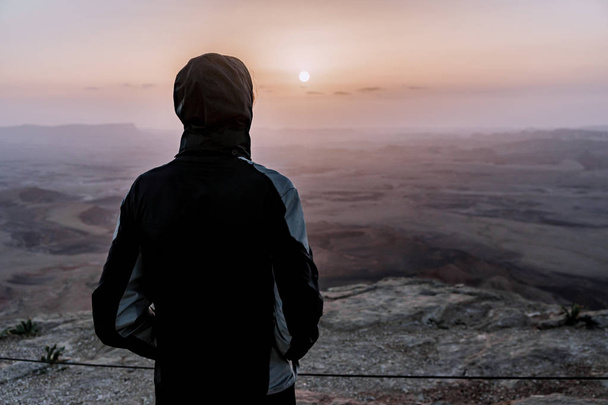 Az ember egyedül Izrael negev sivatagán csodálja a napfelkeltét kilátás. Fiatal férfi személy áll, a szikla szélén - Fotó, kép