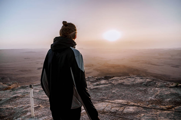 Sám muž v Izraeli Negevské poušti obdivuje pohled na východ slunce. Mladý muž osoba stojí na okraji útesu - Fotografie, Obrázek