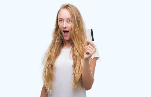 Adolescente rubia sosteniendo tarjeta de crédito asustada en shock con una cara sorpresa, asustada y excitada con expresión de miedo
 - Foto, imagen