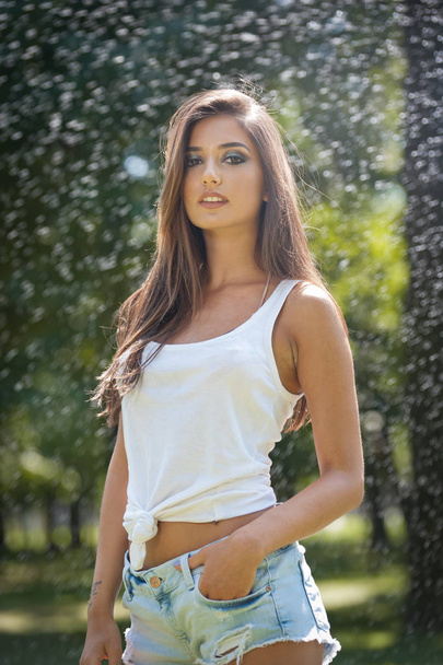 Portrait of sexy woman in spray of water with white T shirt .She has a good gentle skin, sensual posture, and she smiles.Happy young woman  in park. Youth lifestyle. Happiness, joy, summer concept. - Foto, afbeelding