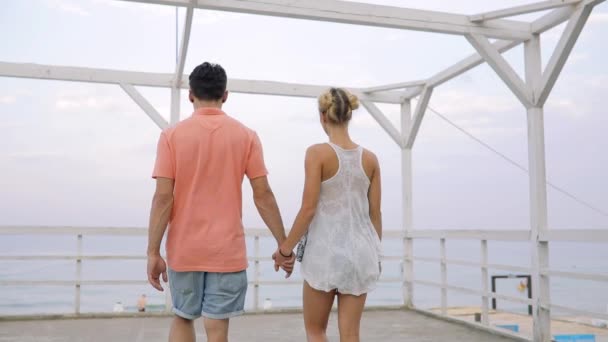 Happy νεαρό ζευγάρι πηγαίνει στη βεράντα στη θάλασσα κρατώντας τα χέρια - Πλάνα, βίντεο