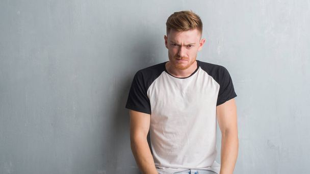 Young redhead man over grey grunge wall depressed and worry for distress, crying angry and afraid. Sad expression. - Foto, afbeelding