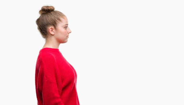 Młoda kobieta blonde noszenie bun i czerwony sweter patrząc w bok, zrelaksować się poza profil z naturalną twarz uśmiech i pewność siebie. - Zdjęcie, obraz