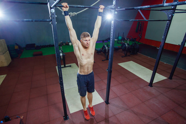 Athlete muscular fitness male model pulling up on horizontal bar in a gym. Cross style fit - Fotó, kép