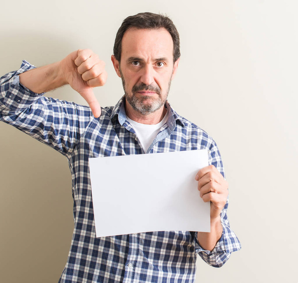 Ανώτερος άνθρωπος κρατώντας φύλλο λευκό χαρτί με θυμωμένο πρόσωπο, αρνητικό πρόσημο δείχνει απέχθεια με αντίχειρες προς τα κάτω, απόρριψη έννοια - Φωτογραφία, εικόνα