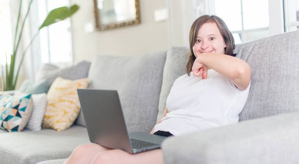 Женщина с синдромом Дауна дома использует ноутбук с неожиданным лицом, указывающим пальцем на себя
 - Фото, изображение