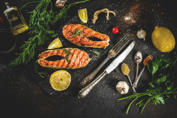 Grilled salmon fish steaks with ingredients lemon, herbs, olive oil, slate cutting board, dark rusty background copy space - Zdjęcie, obraz