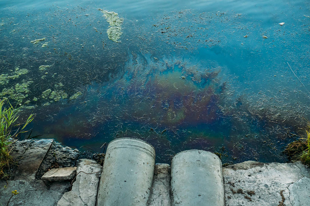 Σωλήνες αποχέτευσης στην ακτή, λεκές πετρελαίου ή καυσίμου στην επιφάνεια του νερού, φύση ρύπανση από τοξικές χημικές ουσίες, βρώμικη θάλασσα - Φωτογραφία, εικόνα