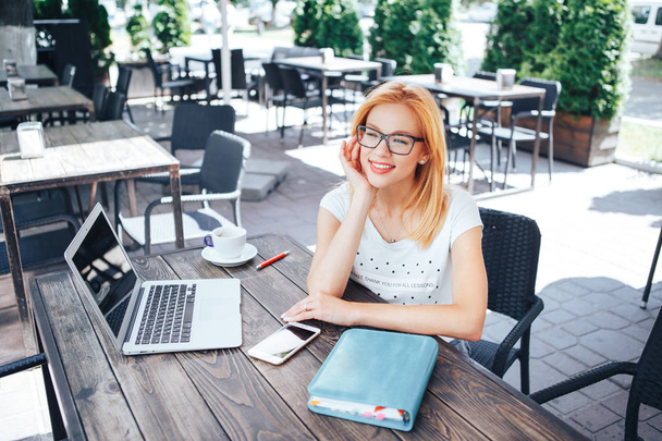 夏のカフェに座っている笑顔若い赤髪の女性。若い女性のカフェで座っているし、ノート パソコンの背後に動作 - 写真・画像