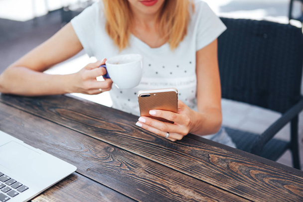 Nahaufnahme eines jungen Mädchens in einem Café, das Kaffee trinkt und das Smartphone betrachtet - Foto, Bild