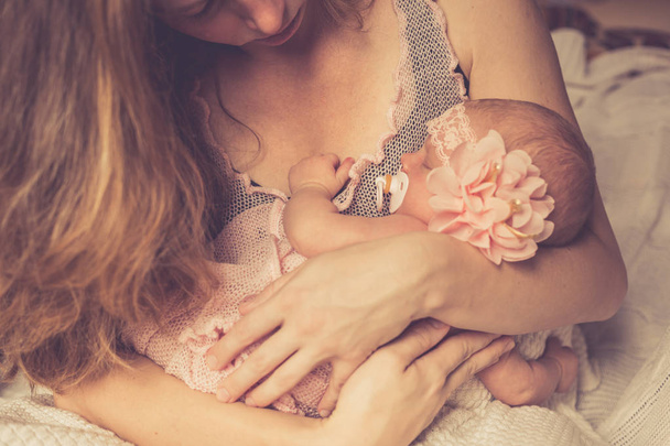 A cute newborn baby girl is sleeping in her mother's arms, who is looking at her. Selective focus. - Фото, зображення