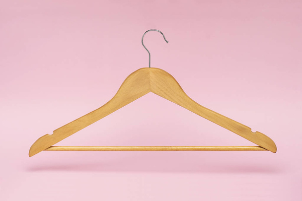 ein Kleiderbügel aus Holz isoliert und wirft Schatten auf rosa Hintergrund - Foto, Bild