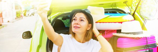 Long banner. Ready to travel. Selfie Woman in Hat before Trip Taking Selfie Green Car Overloaded Things. Bright Suitcases Luggage Accessories Clothes. Summer Concept Holiday Adventure - Foto, imagen