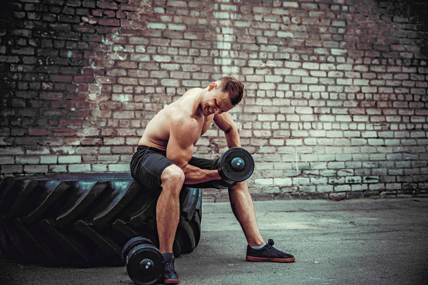 Muscular guy doing exercises with dumbbell against a brick wall - Foto, immagini