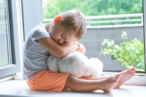 chlapec ze dvou let seděl u okna a objetí hračka králíček. deštivé počasí, čekání na tatínka domů z práce - Fotografie, Obrázek