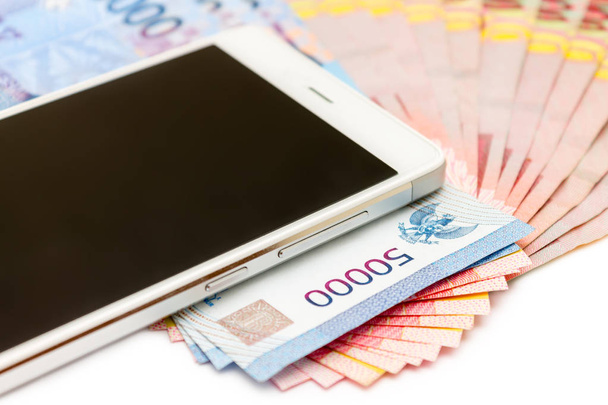 Smartphone powyżej stosy banknotów Indonezja Rupiah (Idr) na na białym tle. - Zdjęcie, obraz