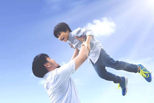 Portrait of young father lifting his son with happy expression under clear sky - Foto, imagen