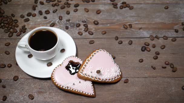 Διατροφής τέχνη. Καλημέρα έννοια. φλιτζάνι καφέ και 2 gingersnaps σχήμα καρδιάς είναι ξύλινο υπόβαθρο. Κόκκους καφέ που έχει πέσει σε αργή κίνηση - Πλάνα, βίντεο