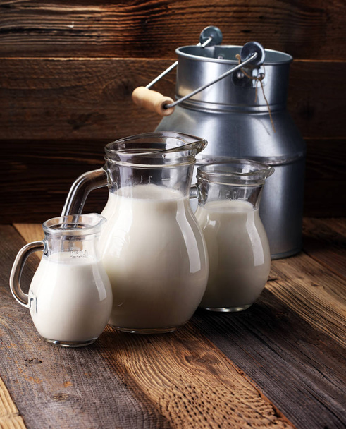 Een kruik van melk en glas melk op een houten tafel. - Foto, afbeelding