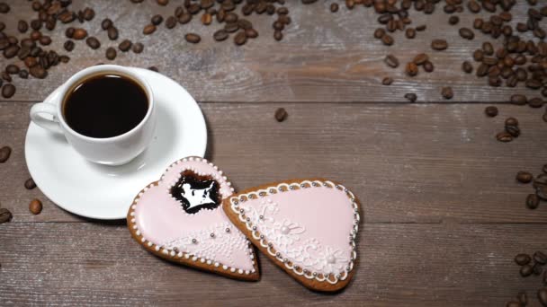 Διατροφής τέχνη. Καλημέρα έννοια. φλιτζάνι καφέ και 2 gingersnaps σχήμα καρδιάς είναι ξύλινο υπόβαθρο. Κόκκους καφέ που έχει πέσει σε αργή κίνηση - Πλάνα, βίντεο
