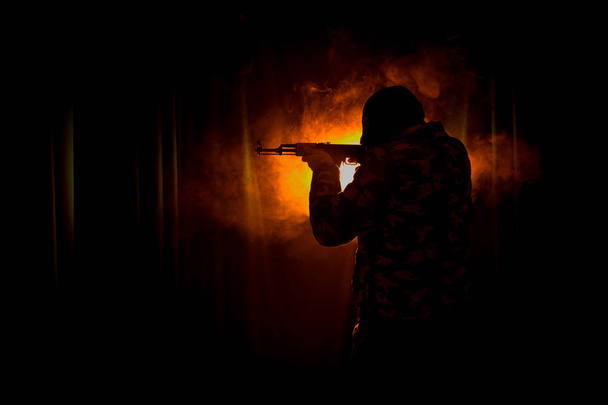 アサルトライフルの暗いトーンの霧の背景や黒着てバラクラバと保有銃手に危険な盗賊に攻撃する準備を持つ男のシルエット。武器のテーマの装飾が施されたテロリストを撮影 - 写真・画像