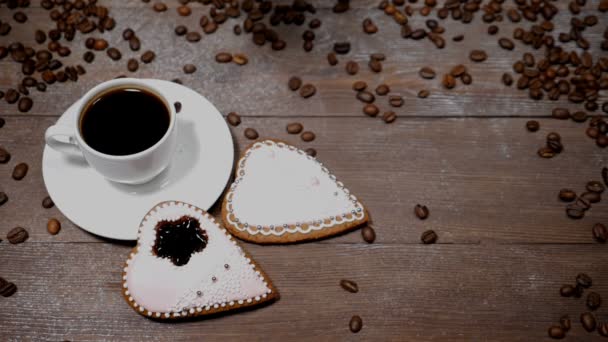 Élelmiszer-art. Jó reggelt koncepció. csésze kávé és 2 szív alakú gingersnaps van a fa háttér. Szemes kávé esik le a lassú mozgás - Felvétel, videó