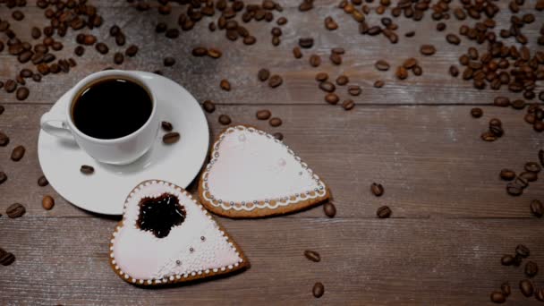 Voedsel-art. Goedemorgen concept. kopje koffie en 2 hartvormige gingersnaps zijn op houten achtergrond. Koffiebonen vallen naar beneden in slow motion - Video