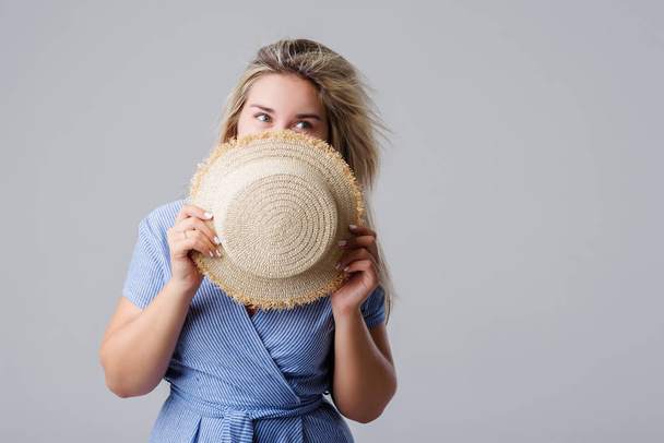 Young blonde woman embarrassed and hides behind a straw hat. Shows only the eyes - Photo, Image