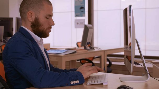 近代的なオフィスで働くカジュアルなスーツを着て大人のビジネスマン。流行に敏感なひげと近代的なオフィス研究職場で座って何かインターネットを利用 - 写真・画像