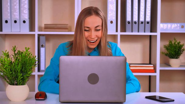 onnellinen työntekijä lukee hyviä uutisia etsivät näytön kannettava tietokone. houkutteleva valkoihoinen blondi istuu pöydän ääressä modernissa pienessä toimistossa
 - Valokuva, kuva
