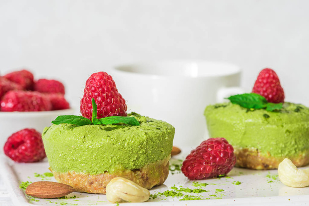 grüner Matcha veganer roher Kuchen mit Himbeeren, Minze, Nüssen und Kaffeetasse zum Frühstück. gesundes, leckeres Essen. Nahaufnahme - Foto, Bild