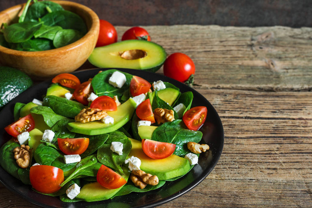 Fresh salad with avocado, spinach, tomatoes cherry, feta cheese and walnuts in a plate on rustic wooden table. healthy food. close up - Zdjęcie, obraz