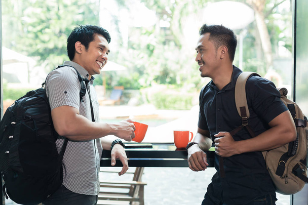 Πλάγια όψη των δύο χαρούμενα νέων ανδρών μιλάμε και πίνοντας τον καφέ  - Φωτογραφία, εικόνα