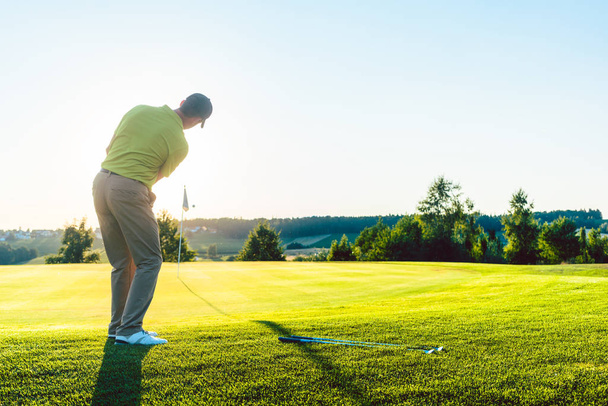 Golfista masculino experiente batendo a bola de golfe em direção ao copo
 - Foto, Imagem
