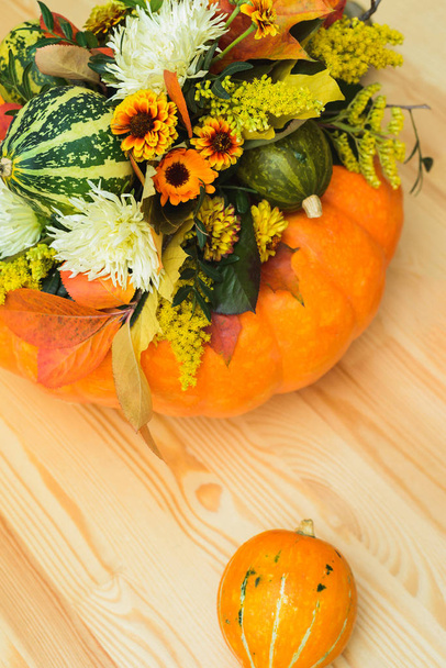 autumn bouquet of decorative pumpkins, flowers and leaves in a vase of orange pumpkin on a wooden table - Photo, Image