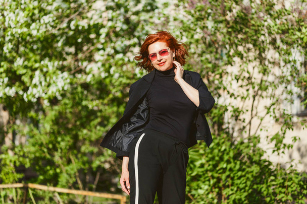 Selbstbewusste rothaarige Frau in schwarzem Anzug und Sonnenbrille im Sommer draußen - Foto, Bild