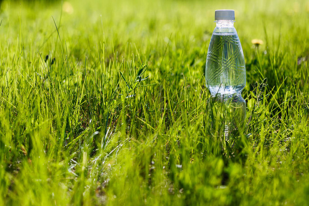 bottle of drinking water stands on the green grass outdoors in summer - Фото, изображение