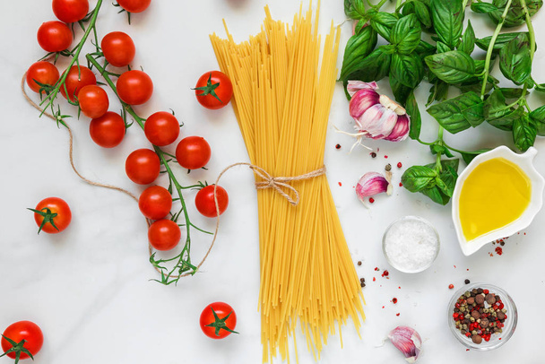 Tészta spagetti paradicsom, fokhagyma, olíva olaj és bazsalikom fehér márvány háttér. Összetevők, a hagyományos olasz étel. szemközti nézet - Fotó, kép