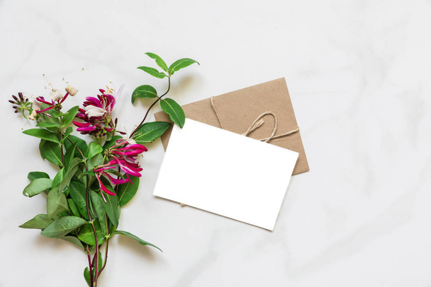 blank white greeting card with pink honeysuckle flowers bouquet over white marble table with copy space. top view. mock up. nature concept - Fotografie, Obrázek